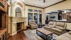 A spacious living room with a fireplace, leather sofas, and a ceiling fan. - Plano Mansion with Beautiful Pool (Plano)