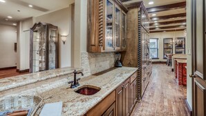 A spacious kitchen with a large island, wooden cabinets, and a stone countertop. - Plano Mansion with Beautiful Pool (Plano)