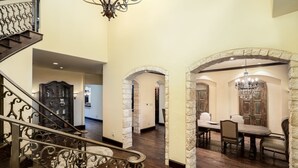 A grand staircase with ornate metal railings leading to a dining area with a stone archway and a chandelier. - Plano Mansion with Beautiful Pool (Plano)