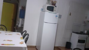 A compact kitchen with a refrigerator, microwave, and stove. There is a dining table with chairs and a patterned tablecloth. - Refúgio da chapada (Cavalcante)