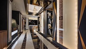 A modern hotel corridor with a reflective black and white marble floor, contemporary lighting fixtures, and a mix of geometric and organic wall designs. - HOTEL K-NEXT (Saitama)