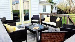 Eine Terrasse im Freien mit Korbmöbeln und einem Tisch, eine gelbe Tür sowie Blick auf ein Nachbarhaus.