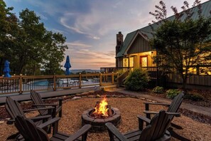Une terrasse en bois avec des sièges d’extérieur, un foyer et une vue sur une piscine et un bâtiment.