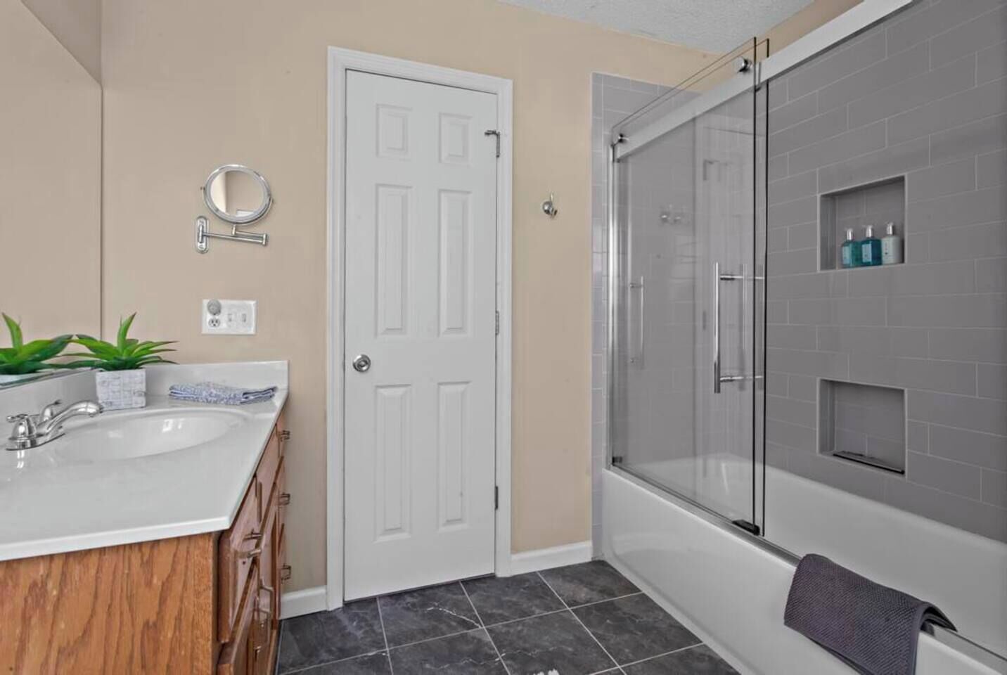A bathroom with a white sink, mirror, and door, a glass shower enclosure, and a towel hanging on the wall.