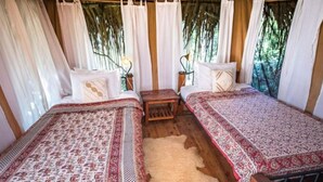 A room with two beds, each with a patterned bedspread, a small wooden table, and a white rug. - Ekorian's Mugie Camp (Sukuta Mugie)