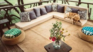 A cozy outdoor seating area with a sofa, cushions, and a small table with a vase of flowers. - Ekorian's Mugie Camp (Sukuta Mugie)