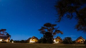 A row of thatched-roof cottages with warm lighting, set against a night sky with stars. - Ekorian's Mugie Camp (Sukuta Mugie)
