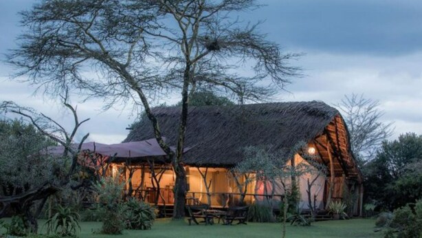 A thatched-roof building with a well-maintained lawn and trees in the foreground. - Ekorian's Mugie Camp (Sukuta Mugie)