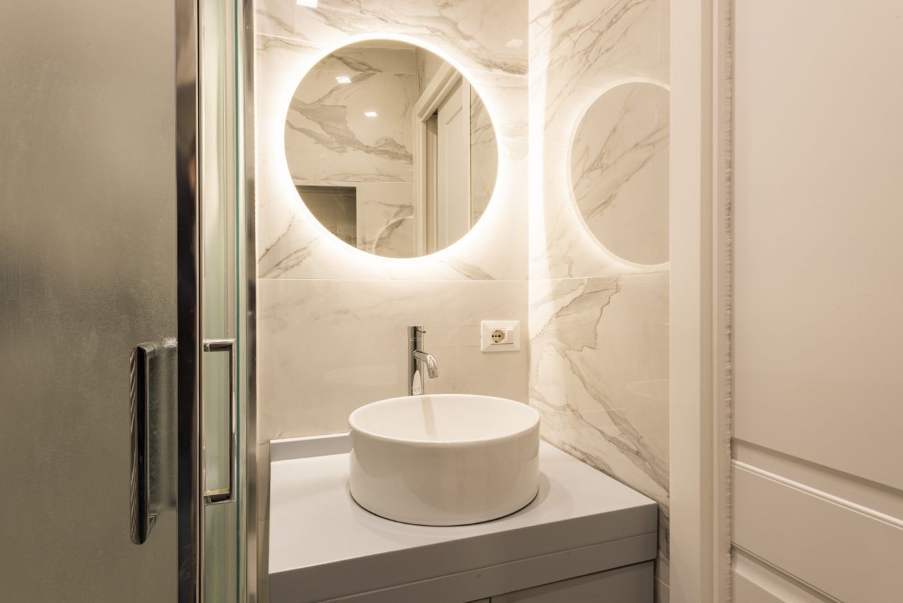 Een badkamer met een ronde spiegel, een wastafel en marmeren wanden.