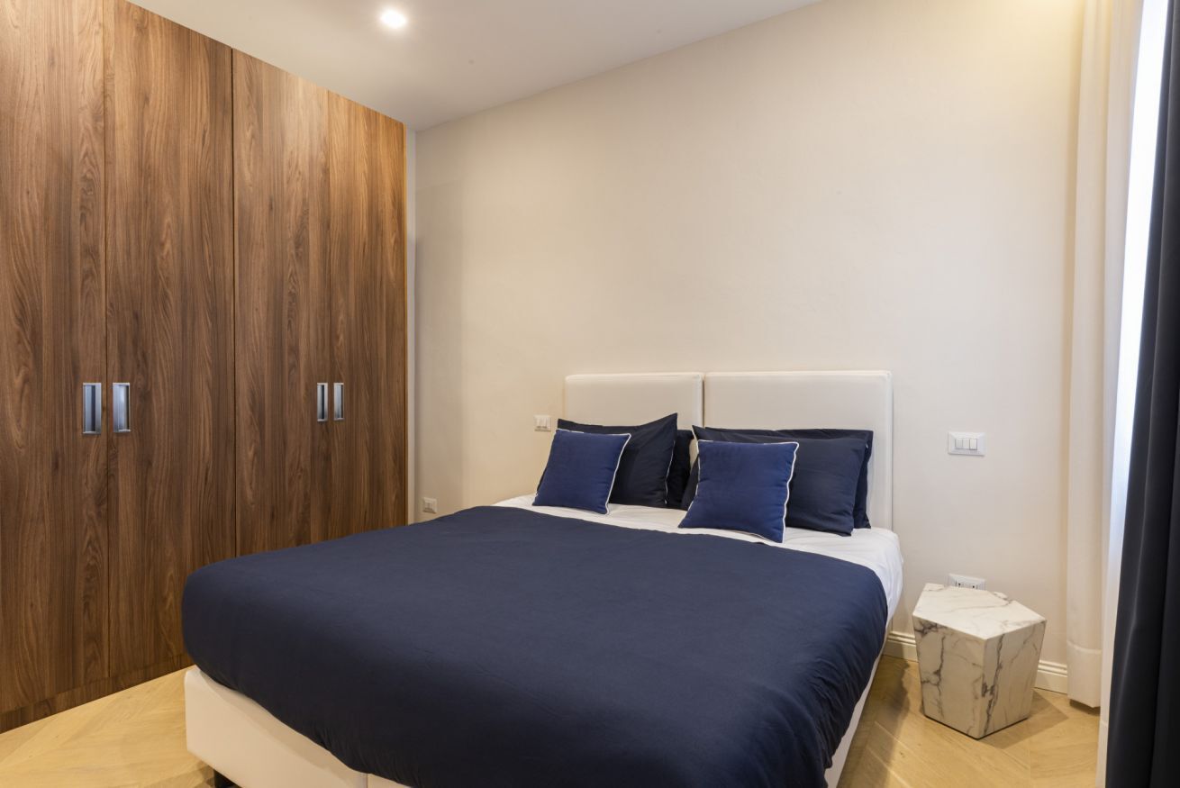 Quarto moderno com cama grande, armário de madeira e mesa de cabeceira de mármore.