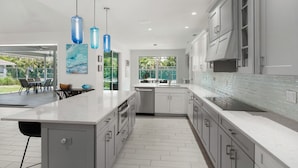 A modern kitchen with a large island, white cabinetry, and blue pendant lights.