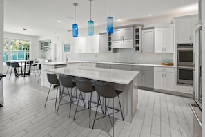Una cocina moderna con una isla grande, taburetes de bar, armarios blancos y electrodomésticos de acero inoxidable.