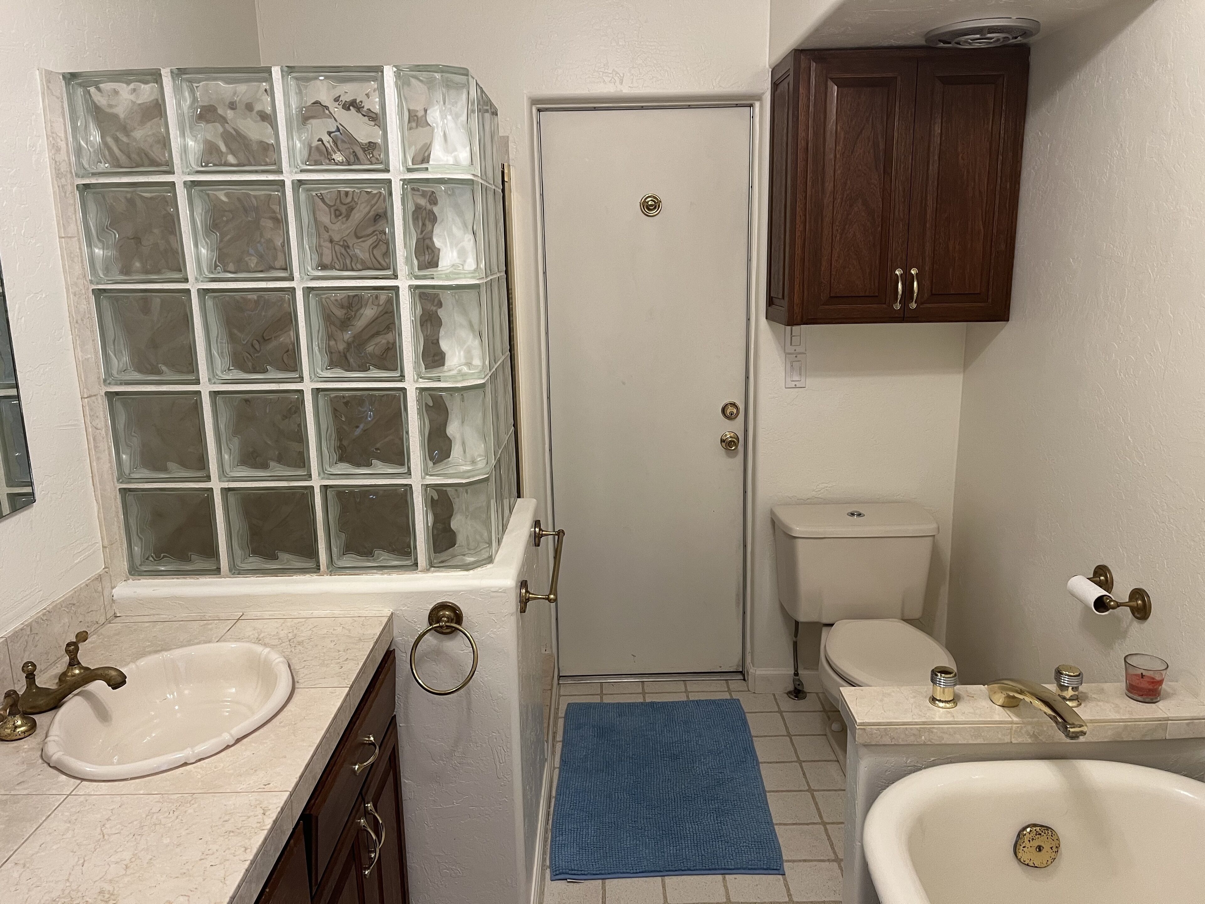 A bathroom with a glass block window, a white toilet, a sink with a vanity, and a bathtub.