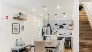 A modern kitchen with a dining area, wooden staircase, and a bench.