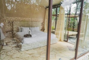 Un dormitorio con pared de piedra, cama con ropa blanca y puerta de vidrio que da a un espacio exterior.