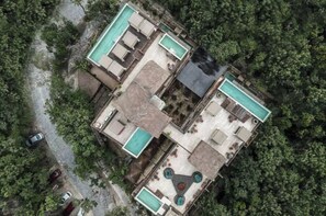 Vista aérea de un resort con varias piscinas, un patio central y vegetación densa circundante.