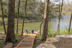 Une jetée en bois avec deux chaises Adirondack bleues, donnant sur un lac paisible entouré d’arbres.