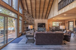 Relax in this spacious living area with a high ceiling and comfortable seating, featuring a large TV and dining space.