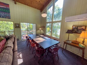 Un comedor con una mesa larga y sillas, ventanas amplias, un ventilador de techo y vistas al exterior.