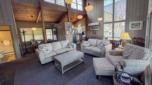 A spacious living area with a high ceiling, large windows, and a cozy fireplace.