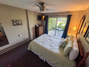 Un dormitorio con cama, ventilador de techo, televisor, cómoda y vistas al exterior a través de una puerta corredera.