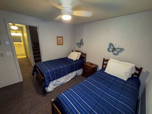 Un dormitorio con dos camas, ventilador de techo y puerta que da a un baño.