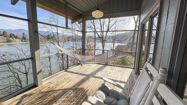 A covered deck with a hammock, a cushioned bench, and a view of a lake and mountains.