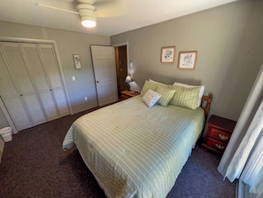 A bedroom with a large bed, a nightstand, a dresser, and a closet.