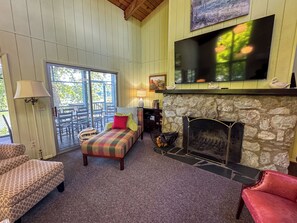 A cozy living room with a stone fireplace, a television mounted above it, and a comfortable seating area with a sofa and chairs.