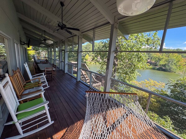 A covered deck with wooden flooring, outdoor furniture, and a hammock.