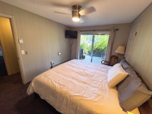 Ein Hotelzimmer mit einem großen Bett, einem Deckenventilator, einem an der Wand montierten Fernseher und Blick ins Grüne.