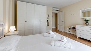 Una habitación de hotel con una cama grande, un armario, una mesita de noche con lámpara, un tocador y un equipo de aire acondicionado.