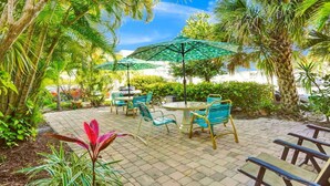 An outdoor patio area with round tables and chairs, surrounded by lush greenery and palm trees.