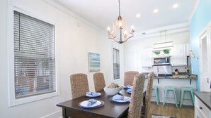 Un coin repas avec une table en bois foncé, dressée pour quatre personnes, entourée de chaises en osier. Un lustre est suspendu au plafond, et les murs de la pièce sont peints en blanc, avec un mur d’accent en bleu.