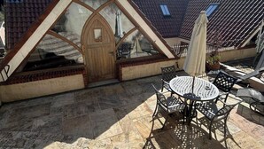 Een terras met een ronde tafel en stoelen, een houten deur en een pannendak.
