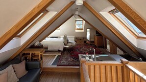 Een knus zolderkamer met een bed, een sofa, een eettafel en een keukenhoek met een spoelbak.