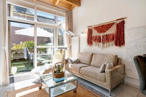 Un salon comprenant un canapé, une table basse en verre, une tapisserie murale et de grandes fenêtres.