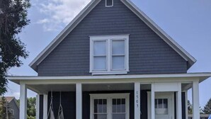 A two-story house with a dark exterior, white trim, and a covered porch with a white fence. - Sunset Motel (Lake City)