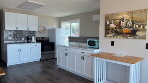 A modern kitchen with white cabinets, a microwave, and a stove. There's a window with a view of the outside. - Sunset Motel (Lake City)