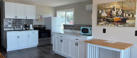A modern kitchen with white cabinets, a microwave, and a stove. There's a window with a view of the outside.