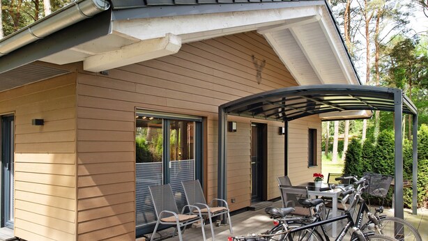 Una casa moderna con un porche cubierto, mobiliario de exterior y bicicletas.