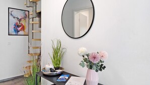 Un mostrador de recepción con un espejo, una obra de arte enmarco, un jarrón con flores y una escalera.