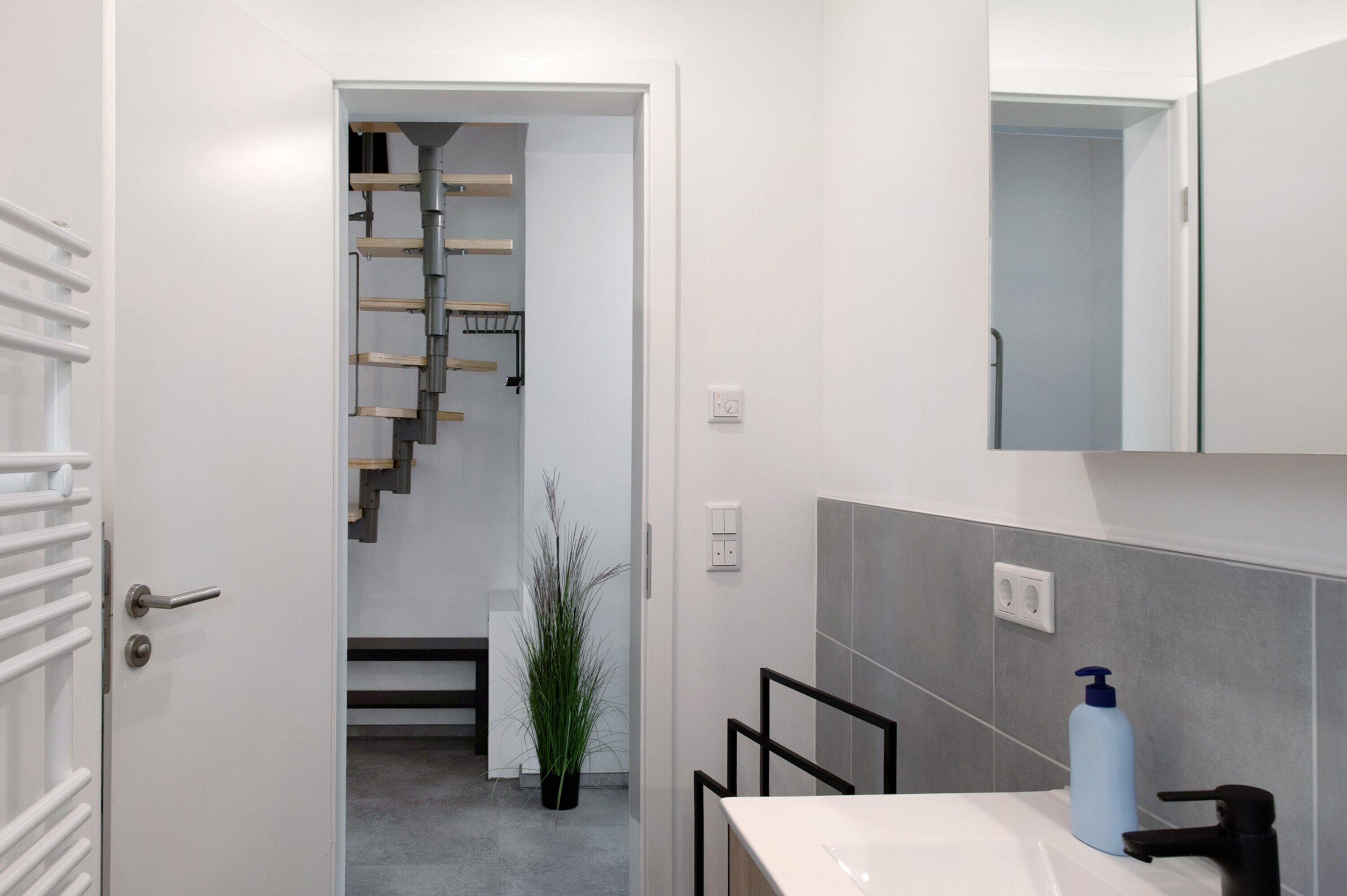 Une salle de bain moderne avec un lavabo blanc, un miroir et un mur recouvert de carreaux gris.