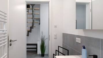 Une salle de bain moderne avec un lavabo blanc, un miroir et un mur recouvert de carreaux gris.