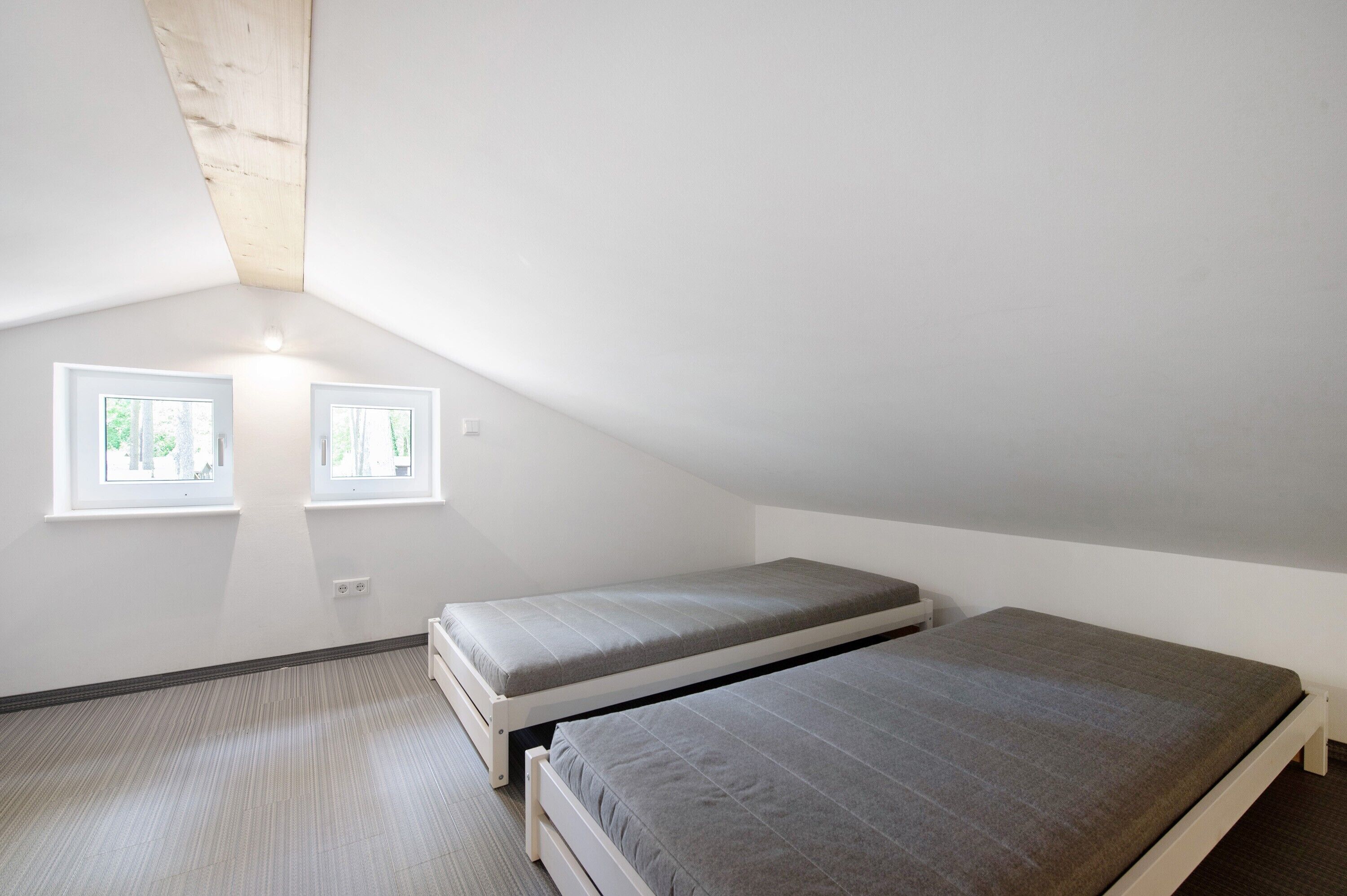 Une petite chambre mansardée triangulaire, avec deux lits simples, des murs blancs et deux fenêtres.