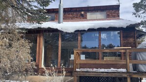 A wooden cabin with large windows, a chimney, and a deck. - Scenic cabin in Carson National Forest (Ranchos de Taos)