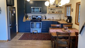 A modern kitchen with dark blue cabinets, a stainless steel refrigerator, a microwave, and a stove. There is a wooden dining table with chairs and a rug on the floor. - Scenic cabin in Carson National Forest (Ranchos de Taos)
