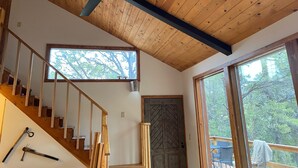 A wooden interior with a ceiling fan, a staircase, large windows, and a door. - Scenic cabin in Carson National Forest (Ranchos de Taos)