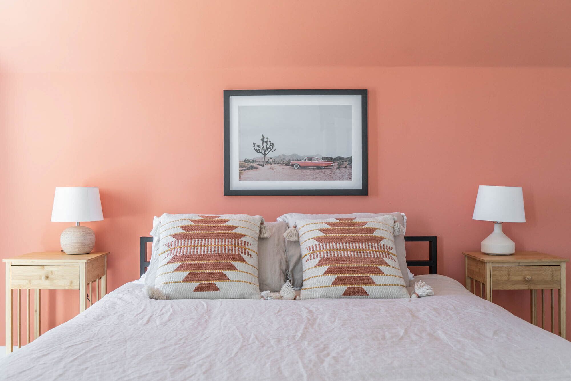 A bedroom with a bed, two nightstands, two lamps, a framed picture on the wall, and patterned pillows.
