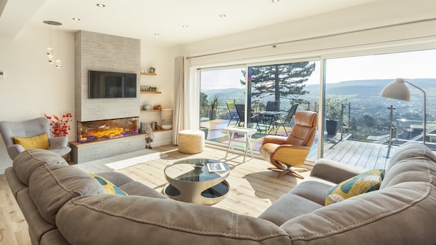 A modern living room with a large sofa, a glass coffee table, and a fireplace. There is a television mounted on the wall, and the room has large windows with a view of the outdoors. - Vikings Annexe, Minehead (Minehead)